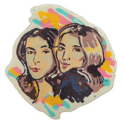 Pancake art depicting two young women with long brown hair posed close together, facing slightly toward the viewer, rendered from approximately the shoulders up against a cream-colored irregular background shape. Bold black outlines define the facial features and hair, with warm peach and tan batte…
