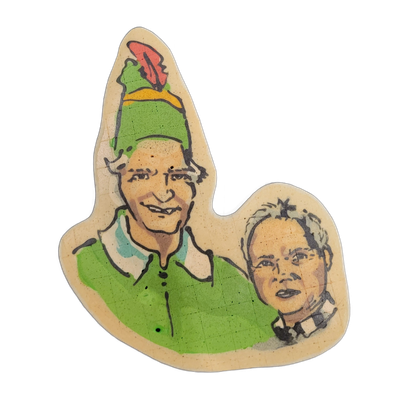 Pancake art depicting two figures: a larger figure in the foreground wearing a tall pointed green hat with a yellow band and red feather, dressed in a green outfit with a teal collar, and a smaller figure in the lower right wearing a black-and-white checkered collar or shirt, with short light-color…