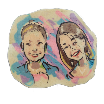 Pancake art depicting two people shown from roughly the shoulders up, side by side, both facing forward and smiling; the figure on the left has hair pulled up into a bun, and the figure on the right has longer hair falling to one side. Bold black outlines define the facial features and hair, with a…