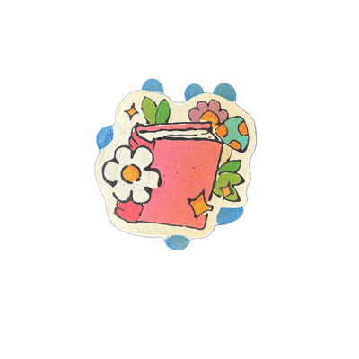 A pink book with white pages visible along the top edge, surrounded by decorative elements including a white six-petal flower with an orange center, green leaves, a purple flower, a teal and orange spotted oval shape, and small four-pointed star shapes in white and yellow-orange, all arranged withi…