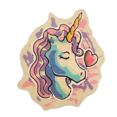 A pancake art piece depicting a unicorn head in profile facing right, with a spiraled yellow and orange horn, closed eye with visible lashes, a small nostril, and a pink heart shape near the muzzle; the mane flows in wavy sections colored in pink, purple, teal, and blue, set against a background of…