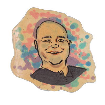 A pancake art portrait of a man with a shaved head, rendered from the shoulders up, wearing a dark gray or black crew-neck shirt, with short visible eyebrows, a slight smile, and light stubble or faint markings along the jawline and chin area. Bold black batter outlines define the facial features a…