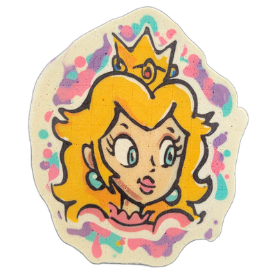 Pancake art depicting a cartoon princess character with voluminous blonde hair, a yellow star-shaped crown with a red gem, teal hoop earrings, large teal eyes, rosy cheeks, and a pink ruffled neckline, surrounded by a splatter-style background of pink, teal, and purple dots and drips on a cream-col…