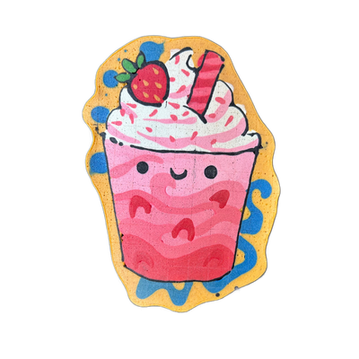 A cartoon-style cup of a pink strawberry drink with a kawaii face, topped with swirled whipped cream, pink sprinkles, a strawberry, and what appears to be a candy stick or wafer roll, surrounded by a yellow border with blue decorative swirl shapes. Drawn by Wella in pancake art using bold black out…