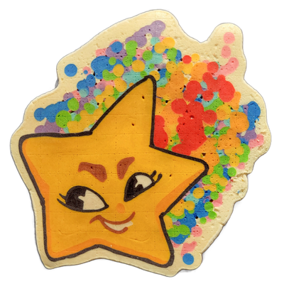 Pancake art depicting Charli, a star-shaped character with a cartoon face, rendered as a five-pointed yellow-orange star with bold black outlines, expressive eyes with lashes, arched brows, a small nose, and a slight smile, surrounded by a loose burst of multicolored dots and splotches in pink, red…