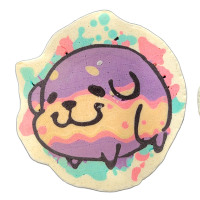 Pancake art depicting Poffridge, a Shiba Inu-shaped poffertje character from the JoP cast, shown as a round face with small ears, a wide nose, and an open-mouth expression, set against a background of loose paint-splatter shapes in teal, pink, and violet on a cream-colored irregular base. The face…