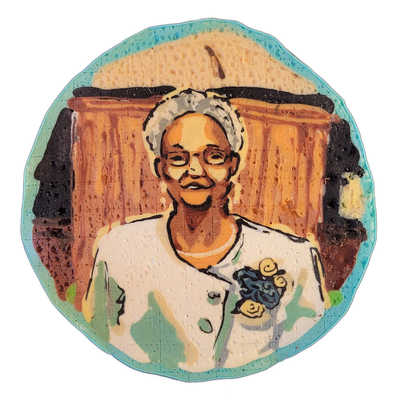 Pancake art portrait of Grandma Gert, depicting a person with short gray-white hair, glasses, and a light-colored jacket with a dark floral brooch, seated in front of what appears to be a wooden headboard or paneled background. The piece uses bold dark outlines with filled areas in warm orange-brow…