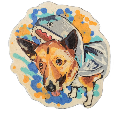 Pancake art portrait of a dog named Bonnie, rendered as a head-and-shoulders view with brown, tan, orange, and black fur markings, pointed ears with dark tips, expressive brown eyes, a black nose, and a pink tongue slightly extended; a large gray fish with an open mouth and visible fins appears beh…