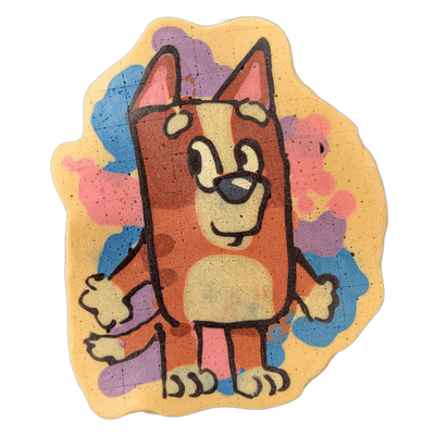 Pancake art depicting Bingo, a cartoon dog character rendered in reddish-brown and tan tones with a cream-colored muzzle and belly, pointed ears, a dark nose, and an upright standing pose with arms slightly extended outward. Bold black outlines define the figure against a yellow background scattere…