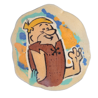 Pancake art depicting a male cartoon caveman figure from roughly the waist up, shown in a three-quarter pose with one arm raised and hand open, wearing a brown animal-skin garment with a stitched cross pattern at the chest, and a yellow bone or clip in his hair; he has a round face, large nose, and…