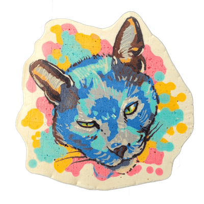 Pancake art portrait of a cat named Murphy, shown from the neck up, facing slightly left, with both ears visible, green eyes, and short whiskers against a cream-colored irregular background filled with scattered circular spots in pink, yellow, and teal. The piece uses bold dark outlines around the…