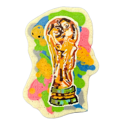 A pancake art piece depicting what appears to be the FIFA World Cup trophy — a gold cup shape with two human figures holding up a globe at the top, mounted on a layered green and gold base — set against a background of irregular color blotches in green, yellow, pink, blue, and gray on a cream-color…