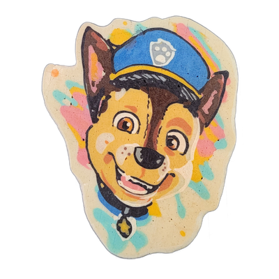 Pancake art depicting the face of Chase, a German Shepherd puppy character from the animated series Paw Patrol, shown from the chest up with a blue police-style cap bearing a paw-print badge, large pointed ears, brown and tan fur markings, wide round eyes, an open-mouthed smile, a blue collar, and…