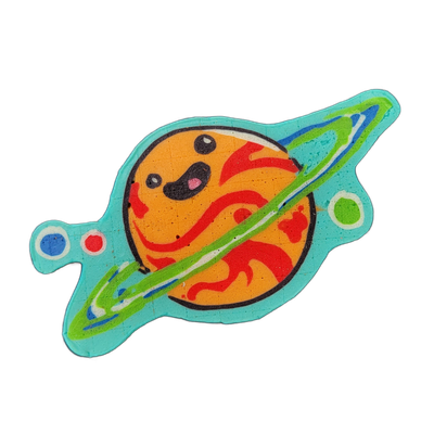 Pancake art of Saturnina, a JoP original character depicted as a round orange planet with a cartoon face — two large black oval eyes, a small open mouth with a pink tongue, and red flame-like swirl patterns across the surface — encircled by a bold green and white ring that passes in front of and be…