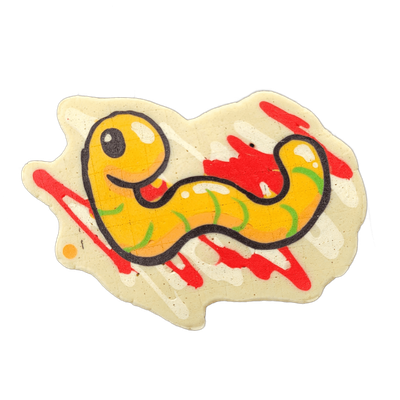 Pancake art depicting Hermie the Wurmy, a cartoon worm character with a large round yellow head, a single circular eye with a small white highlight, a small open mouth with a red tongue, and a sinuous yellow-orange body tapering into a curved tail, decorated with green curved markings along the und…