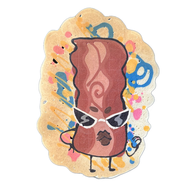 Pancake art depicting Sugar, a JoP original character rendered as an anthropomorphic bacon strip with a tall, wavy body, wearing white cat-eye sunglasses, with small arms, legs, and an open mouth; the figure is shown in shades of brown and reddish-brown against a scallop-edged oval background scatt…