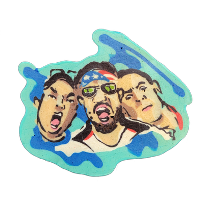 Pancake art depicting three cartoon-style human faces arranged side by side, each with an open mouth and exaggerated expression; the center face has dark skin, a beard, green-lensed sunglasses, and a red, white, and blue star-patterned bandana, while the left face has lighter skin and dark hair, an…