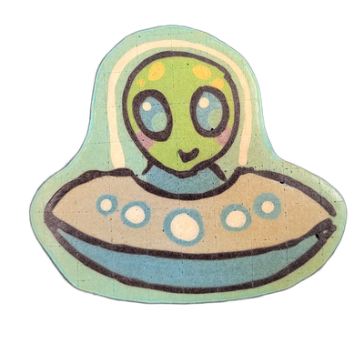 Pancake art of Trav, a round-headed green alien character seated inside a flying saucer with a domed transparent canopy, large blue oval eyes, rosy cheeks, small smile, and yellow spots on the top of the head. Rendered by Dan with bold dark outlines and flat color fills in green, blue, tan, and cre…