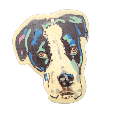 Pancake art depicting the face of a dog, shown from the front, with a white blaze running down the center of the muzzle and forehead, dark markings covering most of the face, and amber-colored eyes. Rendered with fine dark outlines and broad fill areas in dark brown-black, with patches of blue, tea…