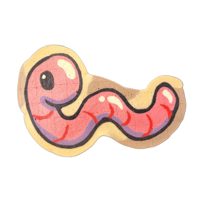 Pancake art of Hermie the Wurmy, a cartoon worm character with a large round pink head on the left, one small dark oval eye, a curved open-mouth smile rendered in purple-toned batter, and a thick sinuous pink body that curves in an S-shape to the right, with short red stroke marks along the undersi…