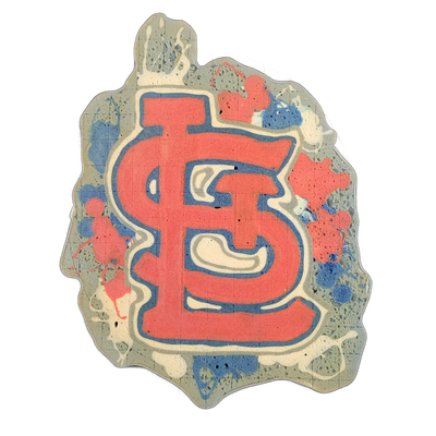 Pancake art depicting the interlocking 'STL' monogram logo associated with the St. Louis Cardinals MLB team, rendered in red and blue on a white background with paint-splatter-style batter drops surrounding the central mark. The logo is outlined in bold blue lines with red fill and white negative s…
