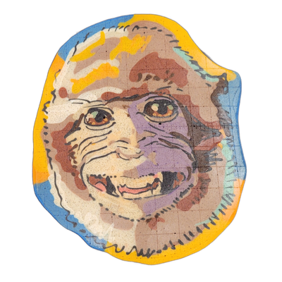 A smiling monkey face rendered in pancake art, shown in a roughly oval shape with an open mouth displaying teeth, forward-facing eyes with amber irises, and a broad nose with visible wrinkles and fur texture lines around the muzzle and cheeks. Fine black batter outlines define the facial features a…