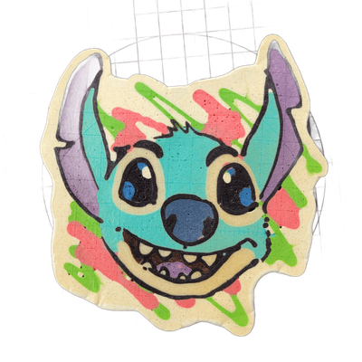 A pancake art piece depicting a cartoon alien creature face with large round eyes with blue irises, a wide open-mouthed grin showing multiple teeth, a broad blue-gray nose, and two tall pointed ears with purple interiors extending upward from the sides of the head. The face is rendered in teal-blue…