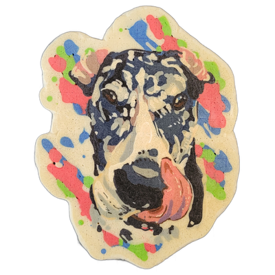 Pancake art portrait of Murphy, a Great Dane, showing the dog's face head-on with a wide open mouth, tongue extended to the lower right, brown eyes, a large black nose, and cropped ears visible at the upper sides of the frame. The face is rendered in bold outlines with layered fills of dark navy an…