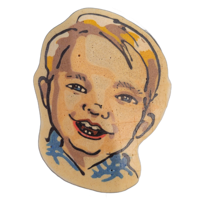 A pancake art portrait of a young child's face, shown from roughly the chin up, with short light brown and golden-yellow hair, blue eyes, and an open-mouth smile showing upper and lower teeth, wearing a blue patterned top visible at the lower edge. The portrait is illustrated with bold dark outline…