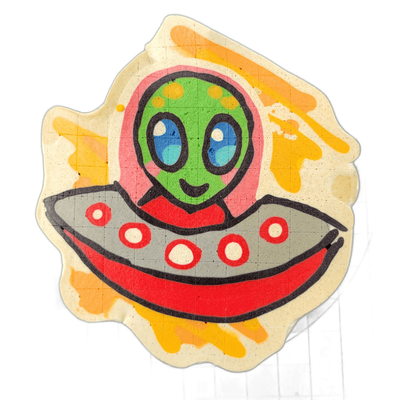 Pancake art depicting Trav, an original JoP character portrayed as a green-skinned alien with large blue oval eyes, yellow spots on the forehead, and a small smile, shown from the torso up inside a gray and red flying saucer decorated with red-outlined white circles along its rim, set against a bac…