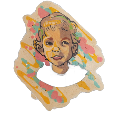 Pancake art portrait of a young child with short light brown hair, facing slightly left, wearing a dark crew-neck top, with a small smile and lips slightly parted. The portrait is rendered with bold black outlines and warm tan batter fill for the face and hair, set against a cream background with s…
