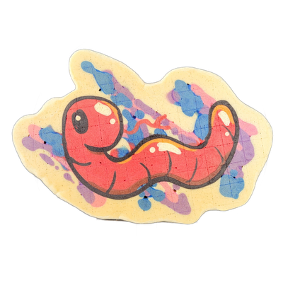 Pancake art depicting Hermie, a worm character from the JoP cast, shown as a rounded, segmented red-orange body with a large circular head, a small eye with a highlight, and a curving tail section that tapers and loops back, set against a cream-colored irregular cloud-shaped background with splashe…