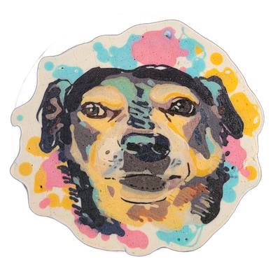 Pancake art portrait of a dog's face centered on a cream-colored, irregularly shaped piece, with the dog's dark fur rendered in bold black outlines and broad fill, brown eyes with white highlight dots, a large dark nose, and floppy ears on either side. Fine and medium-weight black lines define faci…
