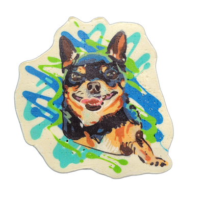 Pancake art portrait of a small black-and-tan dog named Peanut, shown from roughly the chest up with one paw raised, mouth open and tongue visible, ears erect, facing forward against a cream background with overlapping blue, teal, and green paint-splash-style shapes radiating outward. Rendered by D…