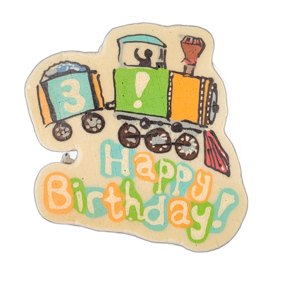 Pancake art depicting a cartoon-style steam locomotive pulling one car, with the number 3 on the car and an exclamation point on the locomotive body, above the text 'Happy Birthday!' in large bubble letters; a small figure appears to wave from the cab, and a red cowcatcher is visible at the front.…