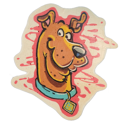 Pancake art depicting a cartoon dog's head and upper neck in profile, facing right, with floppy ears, wide eyes, an open mouth showing teeth, a light blue collar, and a square tag hanging from the collar; the background behind the dog features red splatter-style brushstroke shapes on a cream-colore…