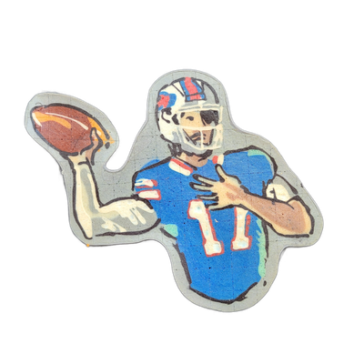 Pancake art of a football player in a blue jersey numbered 11, wearing a white helmet with red and blue markings that include a charging buffalo logo, shown in a passing stance with the right arm raised and holding a brown football.