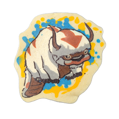 Pancake art of a large, stocky, horned creature with white and gray fur, brown facial markings, a broad flat snout, and six legs, shown in a low crouching or charging pose facing right, with its tail curling upward behind it; the figure is rendered with bold black outlines, white and gray batter fi…