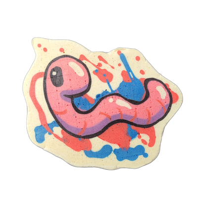 Pancake art depicting Hermie, a worm character from the JoP cast, rendered as a plump, cartoonish worm with a round head featuring a single large dark eye, a small open mouth, and a sinuous body that curves and tapers toward the right. The piece uses bold black outlines with a pink and purple fill…