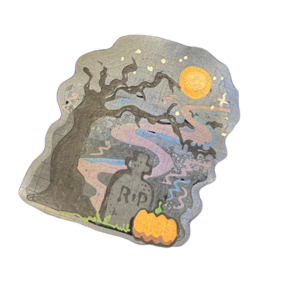 A Halloween-themed pancake art scene featuring a bare, gnarled tree on the left, a tombstone with the text 'RIP' in the center-left, flying bats on the right, a full moon in the upper right, small stars scattered across the upper area, a winding path rendered in pink and blue tones cutting through…