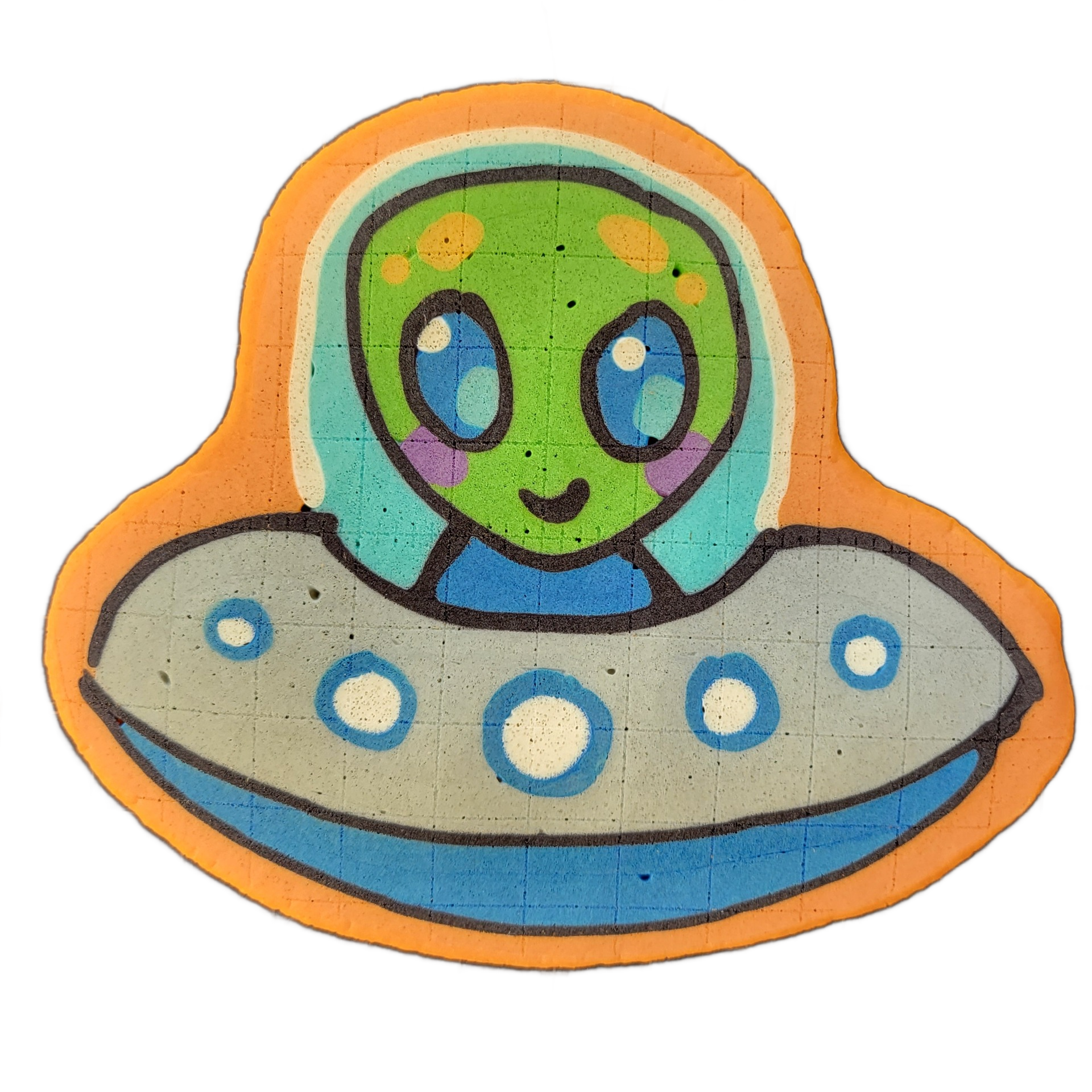 Pancake art depicting Trav, a green-skinned cartoon alien with large blue oval eyes, purple cheek markings, and a small curved mouth, seated inside a gray flying saucer with a domed blue-tinted cockpit canopy and a row of five circular porthole lights along the saucer's rim; the alien wears a blue…