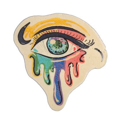 A stylized human eye with a yellow brow line above it, multicolored iris with a white highlight, and heavy dark upper and lower eyelid lines rendered in pancake art on a cream-colored background; below the eye, streams of color in green, teal, blue, purple, and pink drip downward in rounded teardro…
