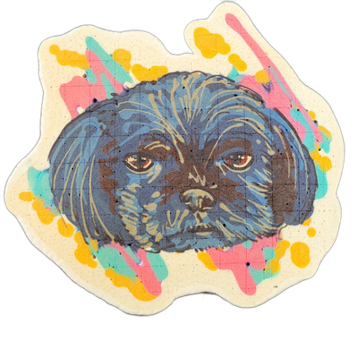 Pancake art portrait of a small, long-haired dog named Smyron, shown from the neck up, facing forward with a flat, round face, brown eyes, a dark nose, and fur radiating outward in layered strokes. The dog is rendered in dark blue, gray, and brown tones with fine batter lines defining individual fu…