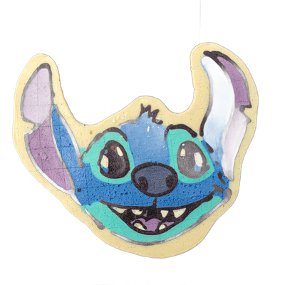 A pancake art piece depicting Stitch, the blue alien creature from Disney's Lilo & Stitch, shown as a close-up face with large brown eyes, a wide open mouth showing small pointed teeth and a pink tongue, a broad dark nose, and two tall rounded ears with purple inner coloring that extend upward and…
