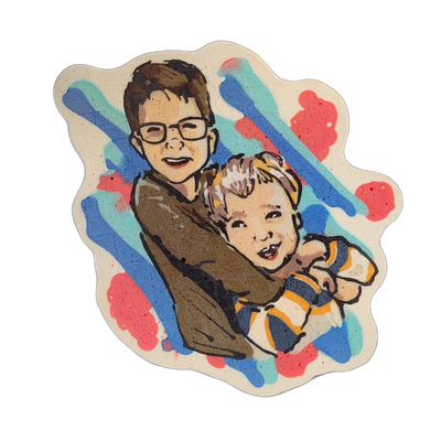 Pancake art depicting two people, Nathan and Owen: an older child or young teen with short dark hair and rectangular glasses holding a younger child with lighter hair and a striped shirt in blue, yellow, and white, both facing forward and smiling. Rendered by Dan with bold black outlines and filled…