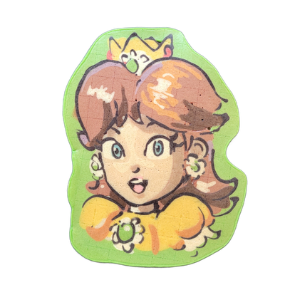 Pancake art portrait of Daisy, a cartoon female character with brown hair styled in large side-swept sections, blue eyes, an open mouth with a surprised expression, flower accessories near her ears, a yellow dress with a ruffled collar, and a green jewel brooch at the neckline; a small yellow crown…