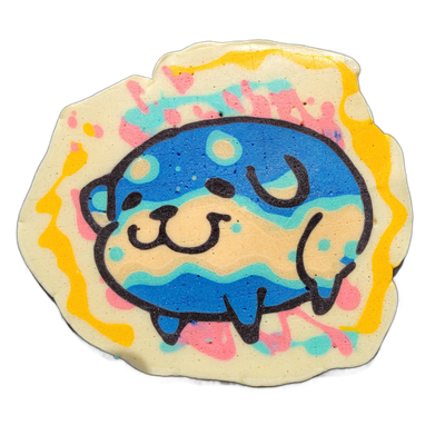 Pancake art depicting Poffridge, a Shiba Inu–shaped sentient poffertje from the JoP cast, shown as a round cartoon face and upper body with small paws, a beige snout with dot nostrils, closed crescent eyes, and a blue rounded head with lighter circular highlights and teal wave patterns across the b…