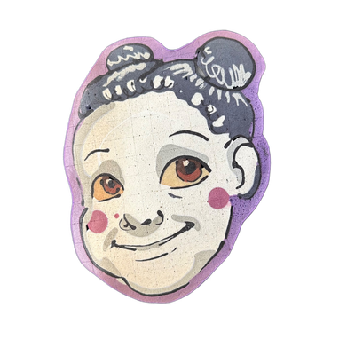 A pancake art portrait of a child's face with short, dark curly hair, brown eyes, rosy cheeks rendered as two pink circles, and a slight smile; the face is pale cream with gray shadow areas, and the hair includes a rounded section on the upper right side of the head.