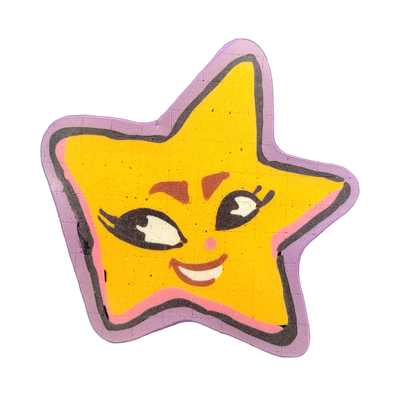 Pancake art depicting Charli, a star-shaped character from the JoP cast, rendered as a five-pointed yellow star with a cartoon face featuring large black-outlined eyes with white highlights, reddish-brown arched brows, a pink dot nose, rosy cheek marks, and a wide smile showing white teeth, bordere…
