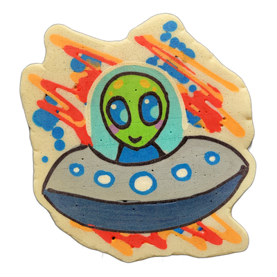 Pancake art depicting Trav, a green-skinned cartoon alien with large dark oval eyes, small dot nostrils, and a slight smile, visible from the torso up inside a domed transparent helmet or bubble canopy, seated in a gray and blue flying saucer with circular porthole details along its rim. The piece…